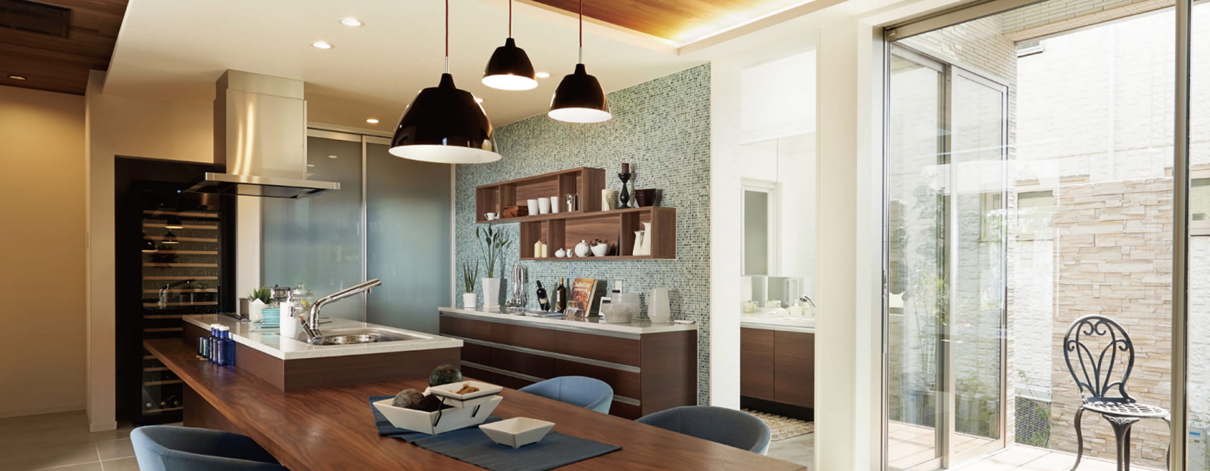 木目調のカウンターとペンダントライトが印象的なダイニングキッチン。奥にはテラスと屋外の椅子が見える開放的な空間